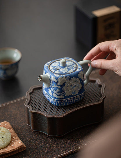 Hand holding the curved handle of a blue peony ceramic teapot
