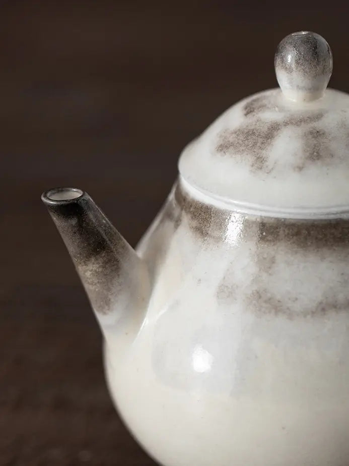 Close-up of the ceramic teapot spout, lid, and charcoal-gray kiln markings