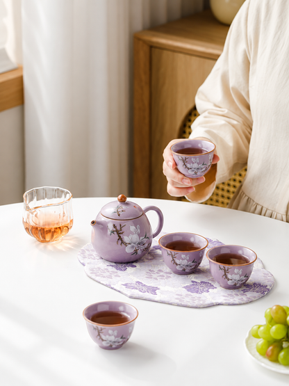Person holding a purple magnolia teacup beside the matching teapot and cups
