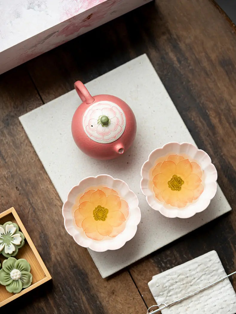 Overhead view of a pink lotus teapot and two blossom-shaped teacups filled with tea
