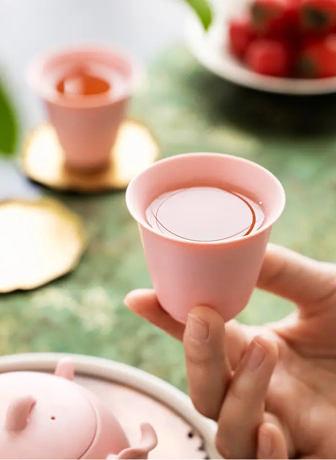 Hand holding a pink zisha tasting cup filled with tea
