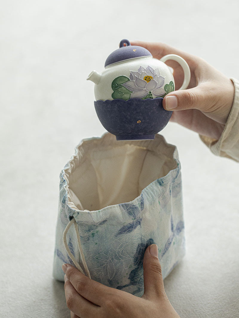 Purple lotus ceramic teapot being placed inside the lined drawstring travel pouch