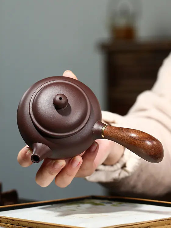 Top view of a handmade Yixing teapot showing the round lid, straight spout and wooden handle