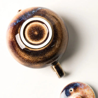 Bottom view of the wood-fired ceramic teapot showing its foot ring, with the lid placed beside it