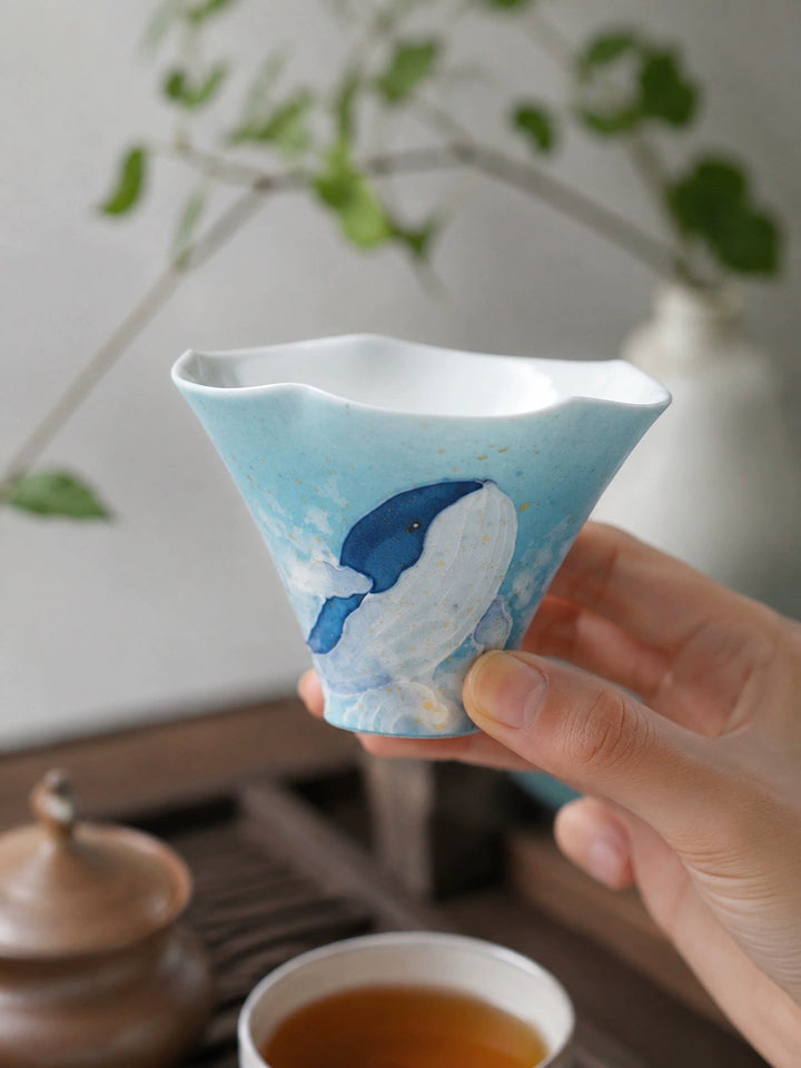 Hand holding the blue whale ceramic tea cup above a gongfu tea table