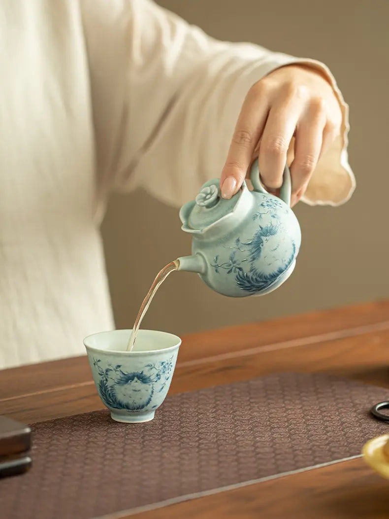 Person pouring tea from the cat ceramic teapot into a matching patterned cup
