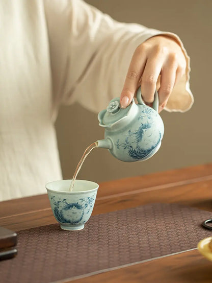 Person pouring tea from the cat ceramic teapot into a matching patterned cup
