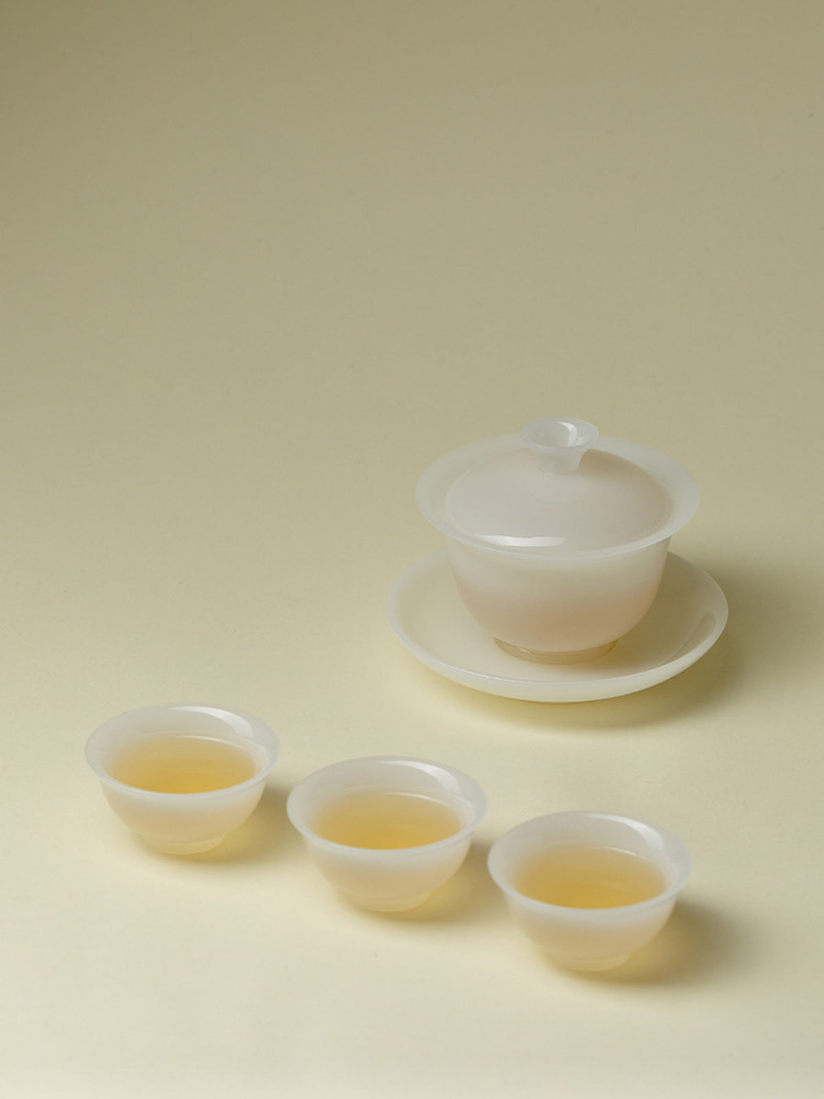 Translucent white gaiwan and three teacups arranged with brewed tea
