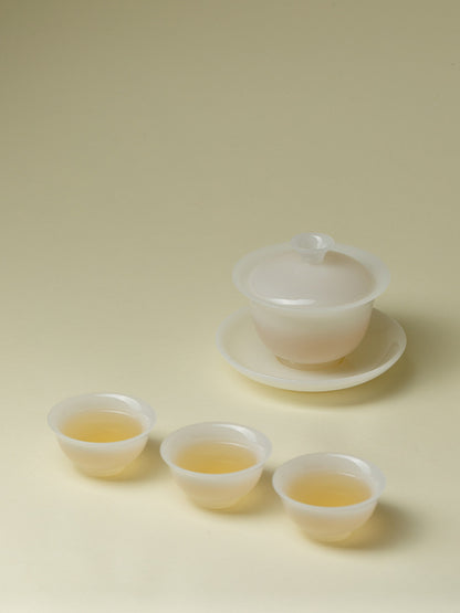 Translucent white gaiwan and three teacups arranged with brewed tea
