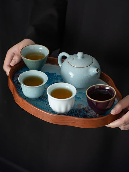 Person carrying the Xishi tea set with four filled tasting cups on a bamboo-framed landscape tray
