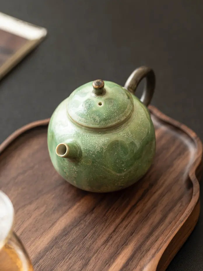 Top-angle view of the green reactive-glaze teapot on a wooden serving tray
