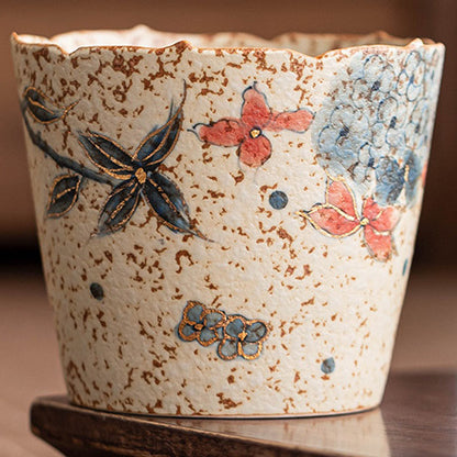 Close-up of blue-gray hydrangeas, red petals, gold-tone outlines, and the naturally speckled ceramic surface