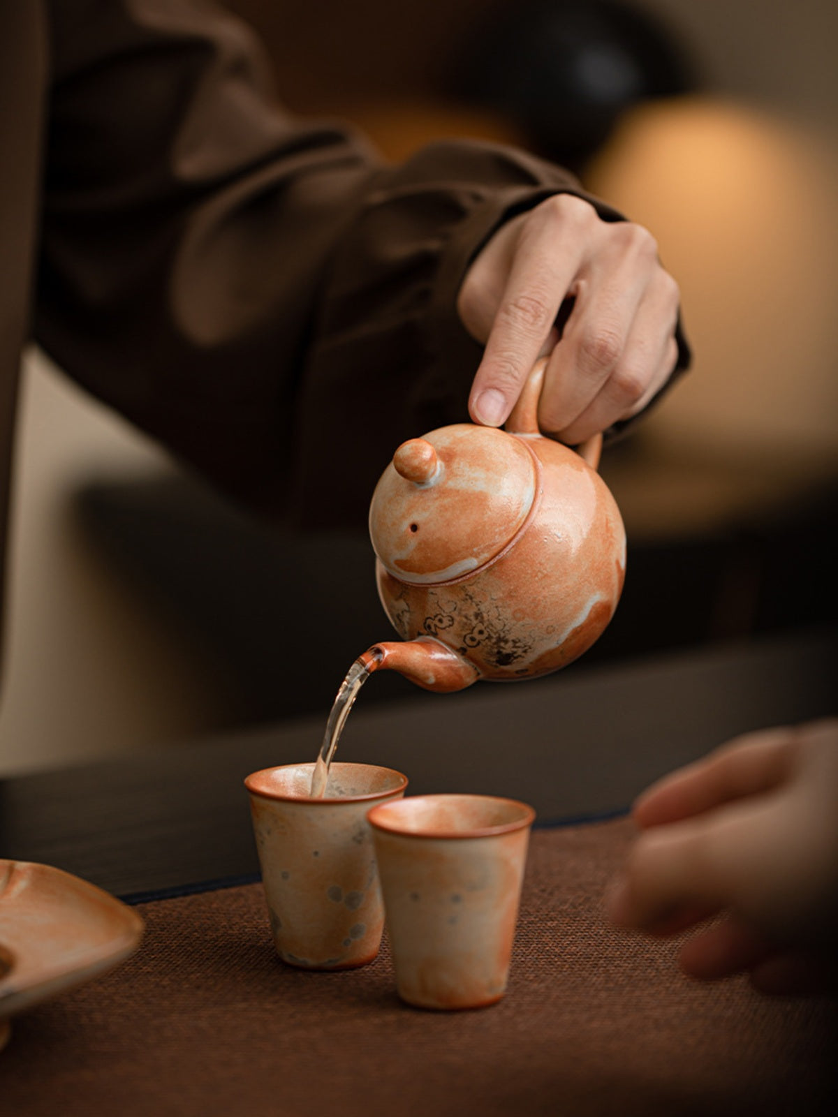 Liting ceramic teapot pouring tea into two small cups in a tea setting