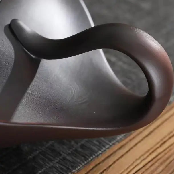 Close-up of the curved loop handle and reddish-brown tonal variation on the zisha teapot