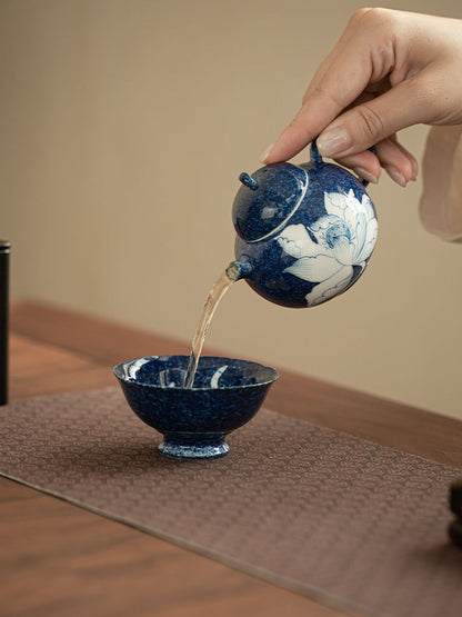 Blue lotus ceramic teapot pouring tea in a warm tabletop setting
