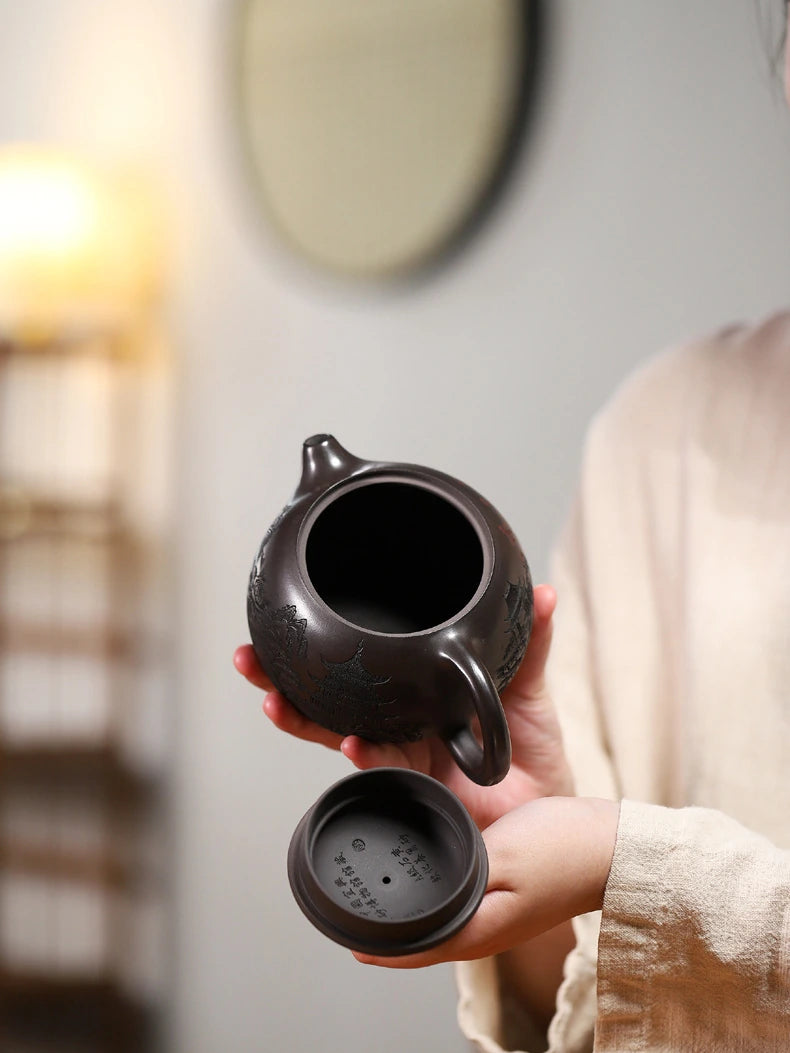 Open Yixing zisha teapot held with its lid to show the wide opening and interior