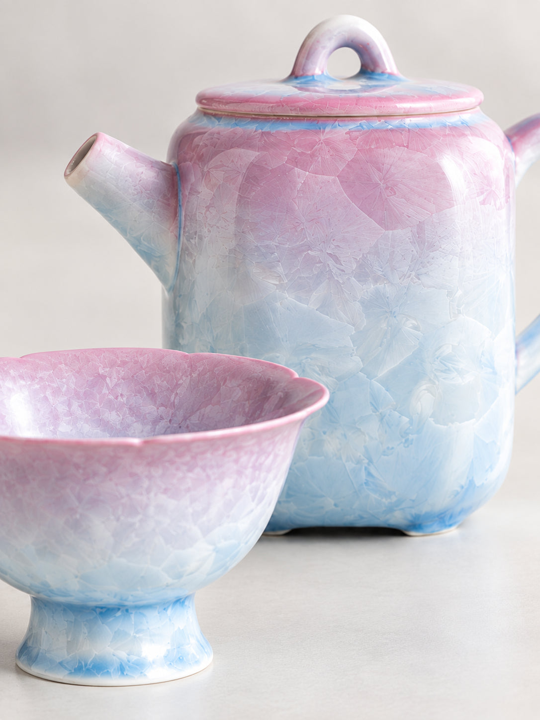 Close-up of the frost-flower crystalline glaze on a pink-to-blue teapot and matching pedestal cup
