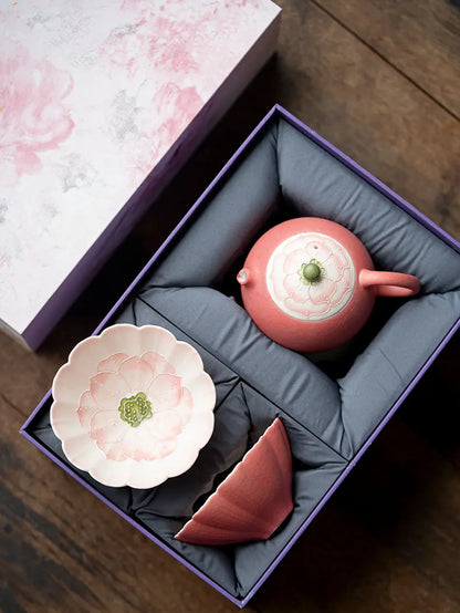 Open pink floral gift box showing the ceramic teapot, one lotus-shaped teacup, and protective padding
