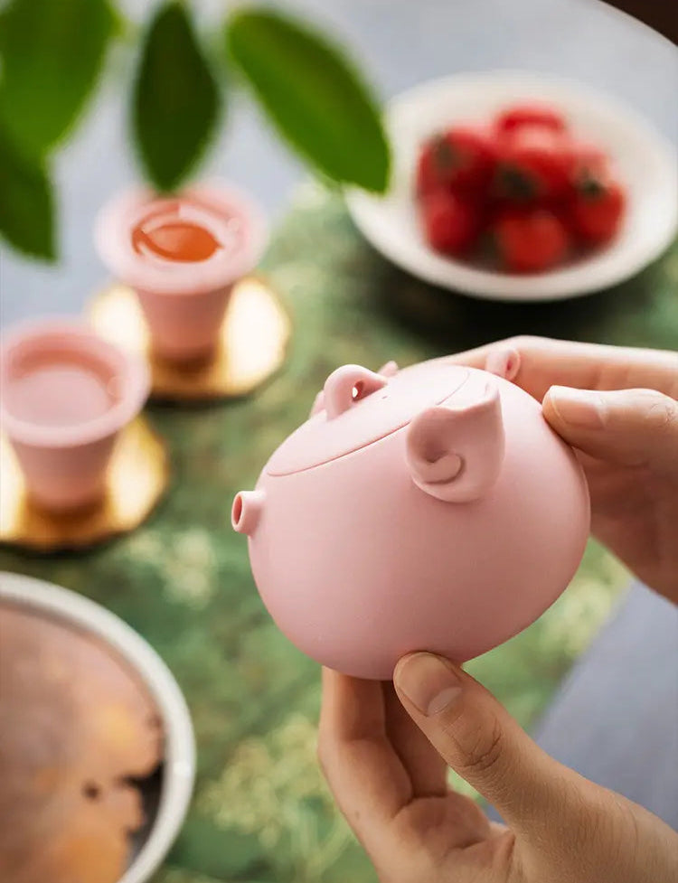Close view of a pink pig-shaped zisha teapot held in both hands