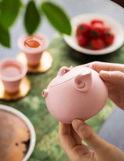 Close view of a pink pig-shaped zisha teapot held in both hands