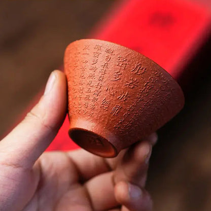 Close-up of a reddish-brown zisha tea cup showing calligraphy and clay texture
