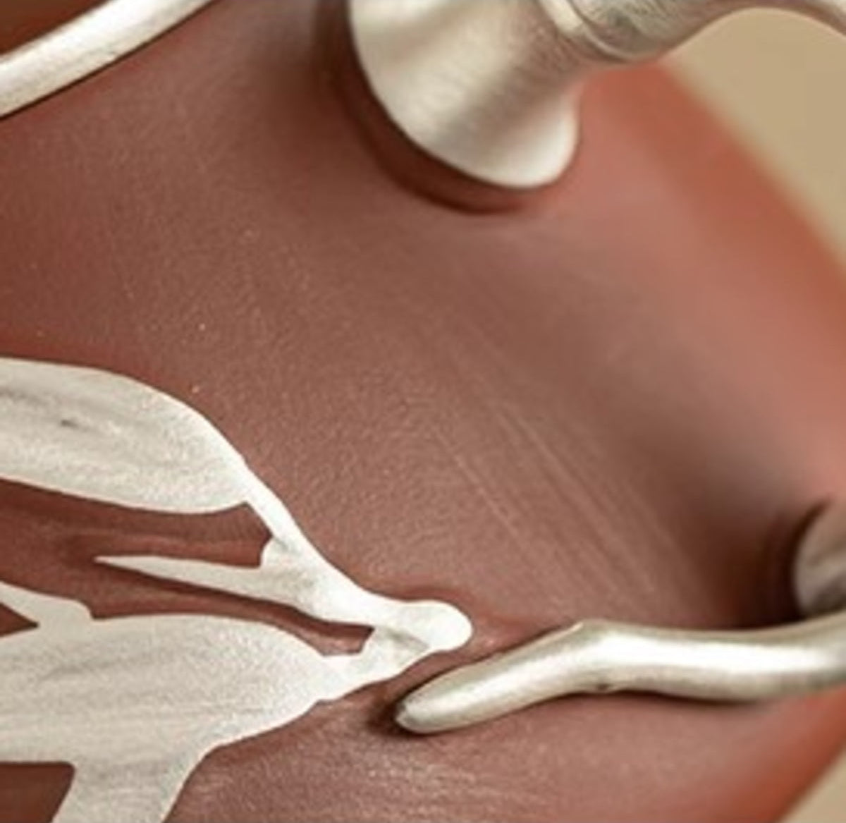 Close-up of silver luster bamboo-leaf and handle details on reddish-brown zisha clay