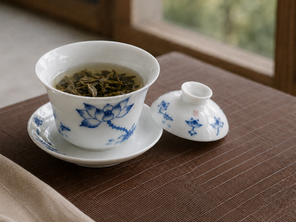 Tea leaves steeping inside the open blue and white gaiwan beside its lid