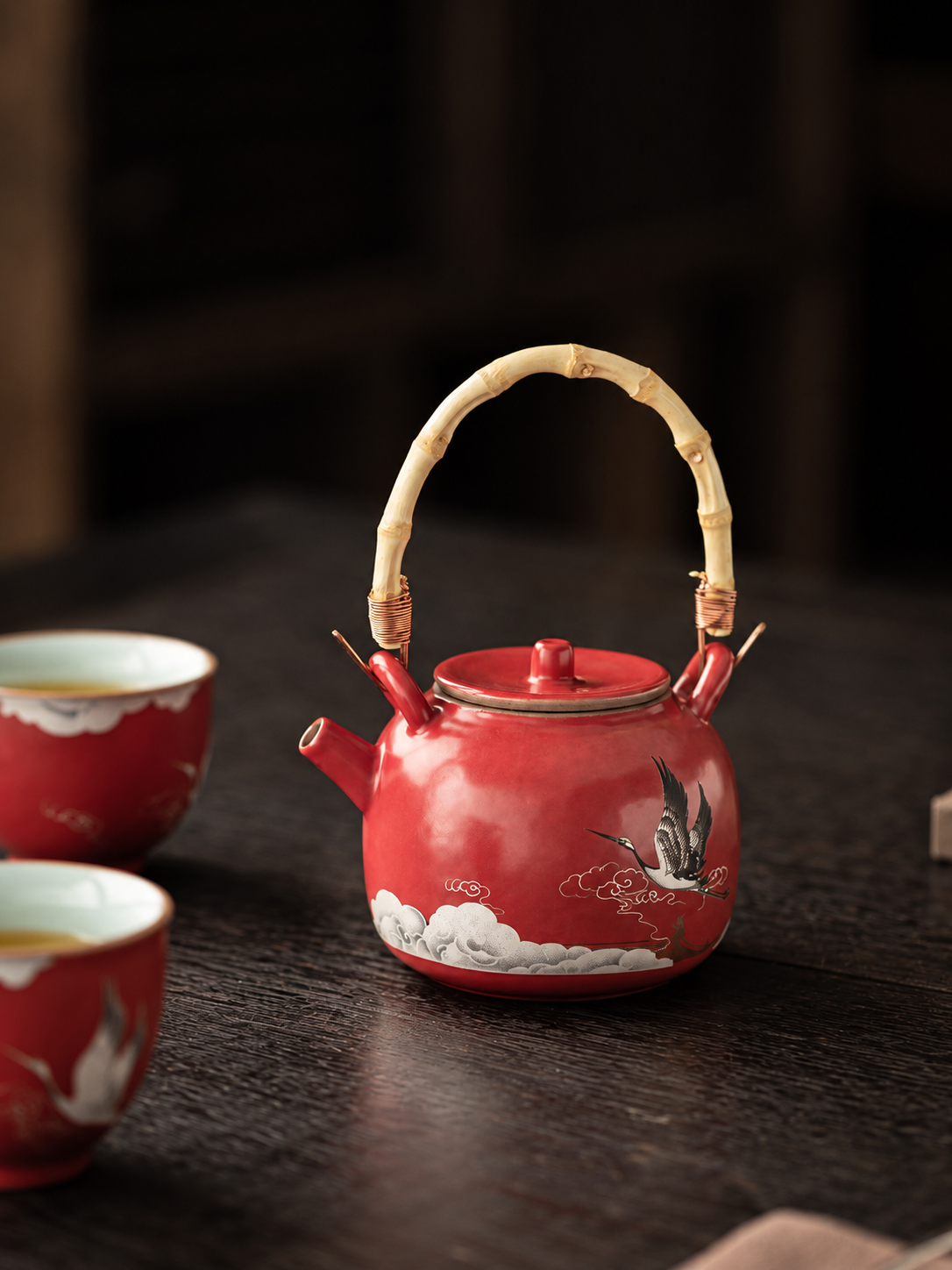 Red crane ceramic teapot with an arched handle displayed on a dark wood table
