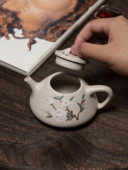 Hand lifting the lid from the floral Yixing teapot on a dark wood table