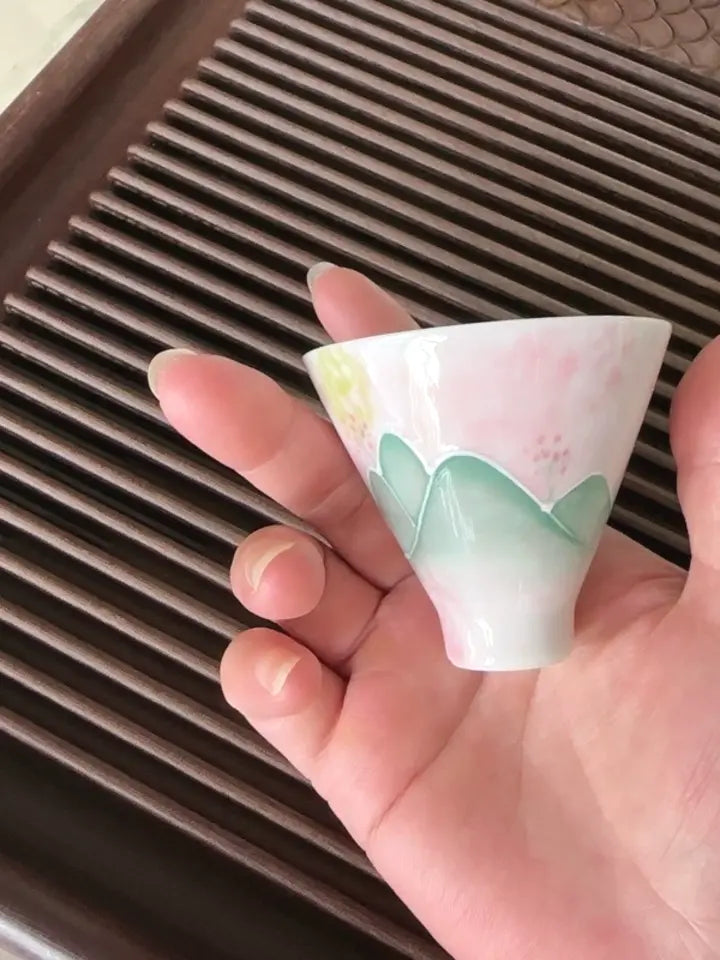 Buyer photo of the blush-green hand-painted landscape teacup held over a wooden tea tray