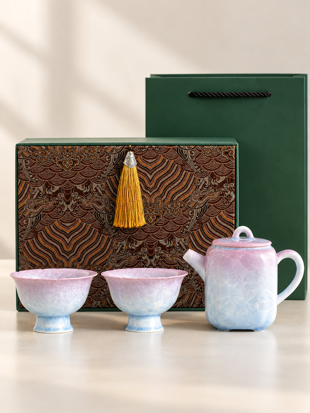 Pink-to-blue crystalline glaze tea set with one teapot and two cups displayed with an example gift box and bag