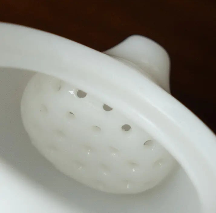 Close-up of the built-in domed multi-hole filter inside a white ceramic teapot
