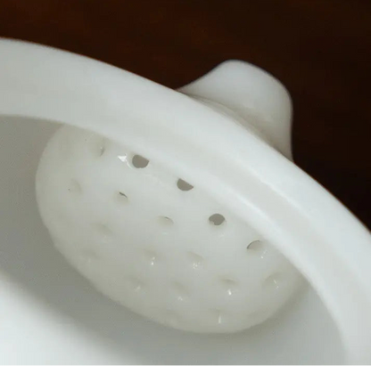 Close-up of the built-in domed multi-hole filter inside a white ceramic teapot
