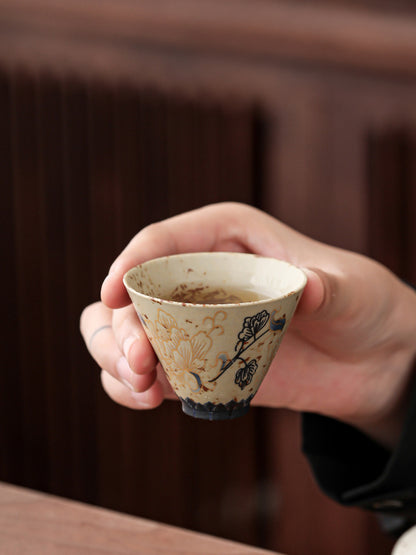 Hand holding a small peony-patterned ceramic teacup
