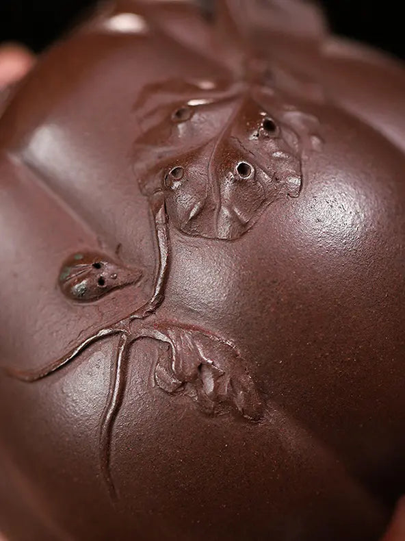 Close-up of raised vine, leaf, and fruit relief on a deep reddish-brown zisha teapot