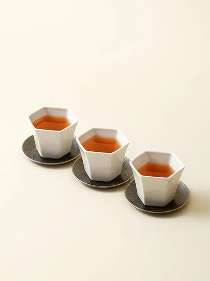 Three white ceramic tasting cups with dark round coasters
