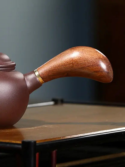 Close-up of the curved wooden side handle and brass-toned collar on the zisha teapot