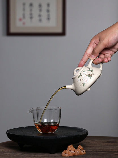 Yixing white duanni teapot pouring amber tea into a clear glass cup