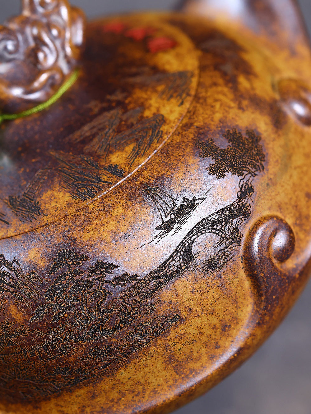 Close-up of the hand-carved riverside landscape with bridge, boat, and trees on the zisha teapot
