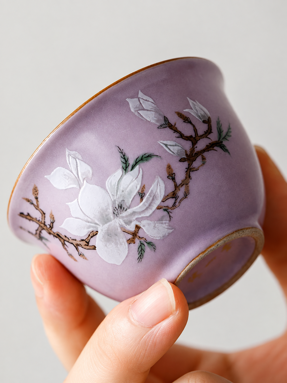 Hand holding a purple teacup with a detailed white magnolia motif
