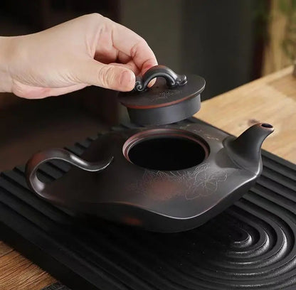 Hand lifting the lid from the carved Yixing zisha teapot resting on a black tea tray
