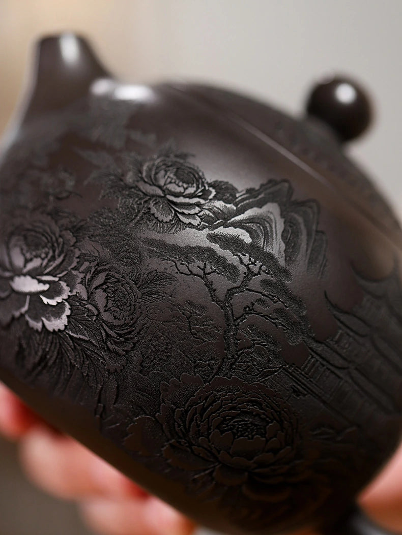 Close-up of peony, mountain, tree, and pavilion carving on the dark zisha clay surface
