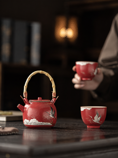 Red crane ceramic teapot and matching cup in a quiet tea setting

