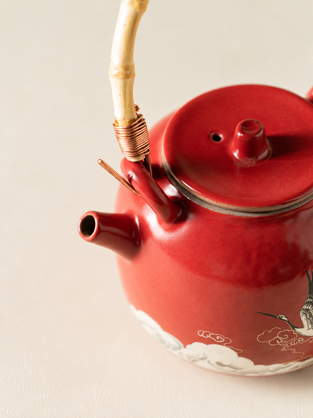 Close-up of the red ceramic teapot lid, spout, and bamboo-style handle binding
