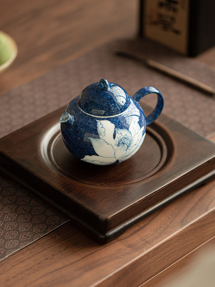 Blue lotus ceramic teapot arranged on a dark wooden tea tray
