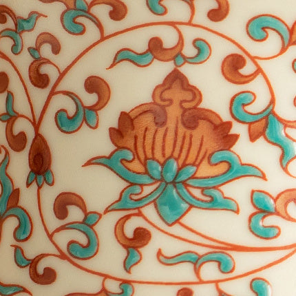 Close-up of the red and green scrolling lotus pattern on the ceramic surface