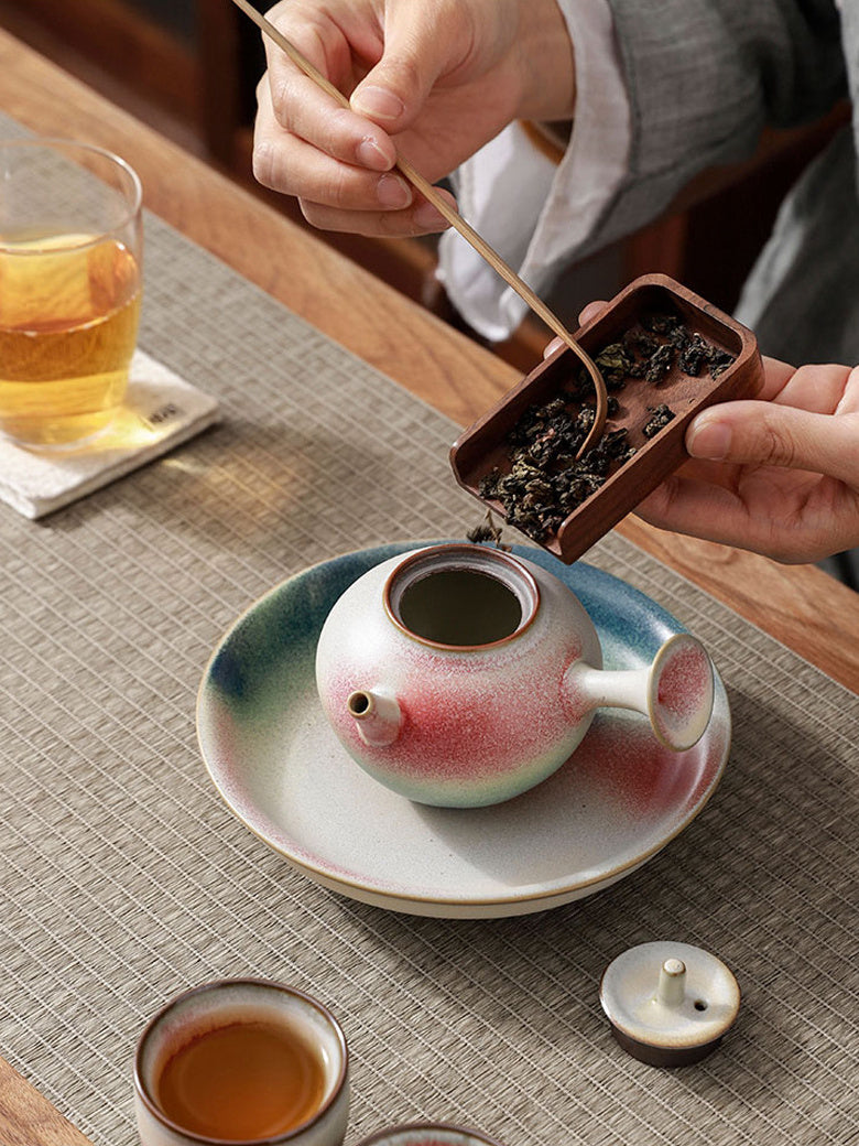 Loose tea leaves being added to an open side-handle ceramic teapot