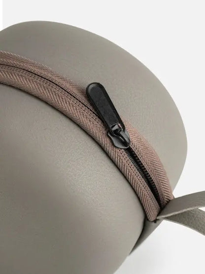 Close-up of the zipper and wrist strap on the round gray carrying case

