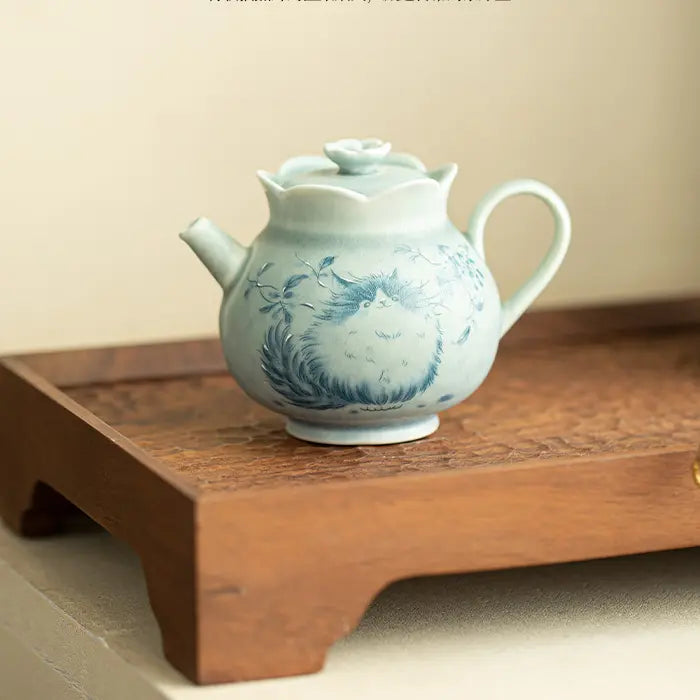 Cat-motif ceramic teapot displayed alone on a carved wooden stand