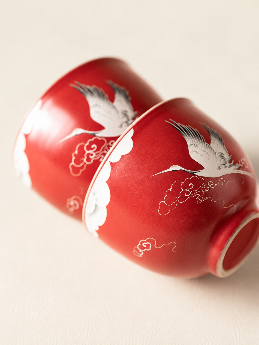 Close-up of raised crane and cloud motifs on two red ceramic teacups

